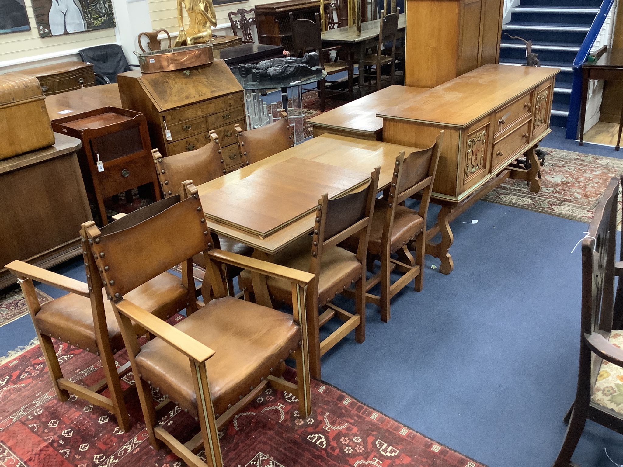 A Maple & Co oak dining suite of Italianate design, with carved and painted decoration and heraldic panels, comprising refectory table, six studded hide-covered chairs, sideboard, two-door cabinet on stand and a side tab